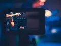 Ręka zamyka klaps filmowy. Na ekranie widać napis "REC:Codec 03:14:07". To plan średni, zapowiadający rozpoczęcie nagrania.