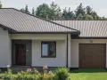 Dom z dachem z blachy trapezowej. Wymiary dachu dopasowane do nowoczesnej bryły budynku. Przed domem ogród z kwiatami.