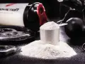 Polvo blanco en una cuchara medidora, junto a pesas y un bote de suplemento. Descubre para qué sirve la creatina y potencia tus entrenamientos.