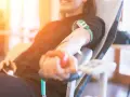 Uśmiechnięta osoba oddaje krew, ściskając czerwoną piłeczkę. Po oddaniu krwi warto pamiętać o nawodnieniu i lekkim posiłku.