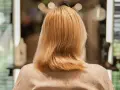 Kobieta z blond włosami, zastanawia się, jak nosić siwe włosy. Włosy są średniej długości, lekko falowane.