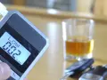 Alkomat z wyświetlaczem pokazującym 0.02% BAC, obok kieliszek z alkoholem i kluczyki samochodowe.