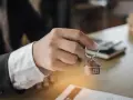 Dłoń trzyma brelok w kształcie domu z kluczem.