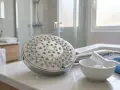 Limpieza de alcachofa de ducha con cal. Cepillo, bol con agua y paño azul listos para ayudarte a como quitar la cal de la alcachofa de la ducha.