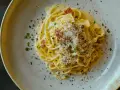 Ein Teller cremiger Spaghetti Carbonara, bestreut mit Pecorino, schwarzem Pfeffer und knusprigen Speckwürfeln.