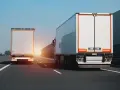 Dwa białe tiry jadą autostradą. Na jednym z nich widać znak zakazu wyprzedzania dla ciężarówek.
