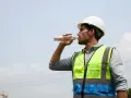 Mann in Warnweste und Helm trinkt Wasser. Hitzefrei auf dem Bau ist wichtig, um hydriert zu bleiben.