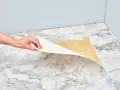 Mano retirando capa de vinilo del suelo. Un paso clave para saber como quitar pintura de caucho del suelo.