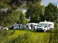 Kilka kamperów zaparkowanych na zielonym trawniku, w otoczeniu drzew. Idealne miejsce na wakacje w kamper park.