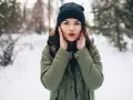 Zastanawiasz się, jaki szalik do zielonej kurtki? Ta dziewczyna w zimowym lesie ma czarną czapkę i zieloną kurtkę.
