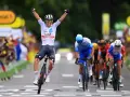 A cyclist in a white UAE Emirates jersey celebrates victory at the Tour de France, arms raised in triumph as he crosses the finish line.