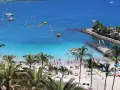Słoneczne gran canaria plaże z palmami, turkusową wodą i ludźmi odpoczywającymi na piasku. Widać łodzie i sprzęt wodny.