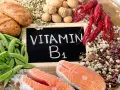 Na tablicy napisano "Witamina B1". Wokół niej znajdują się łososie, raki, fasole, orzechy, pestki i pieczywo.