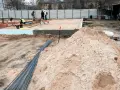Budowa w marcu 2026. Działka z uregulowanym stanem prawnym, przygotowana pod fundamenty. Piasek, zbrojenie i pracownicy na placu budowy.
