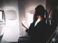 Kobieta w okularach trzyma telefon, zastanawiając się, czy w samolocie jest wifi. Obok ekran rozrywki.
