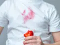 Dziecko trzyma kawałek truskawki, a na białej koszulce widać czerwone plamy z truskawek.