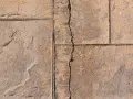 A prominent crack runs through a stamped concrete slab foundation, revealing sand and smaller fissures.
