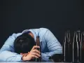 Mężczyzna w niebieskiej koszuli opiera głowę na rękach, obok niego leży kilka pustych butelek po piwie. To obraz utraty kontroli nad piciem.