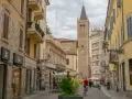 A man cycles down a street in Parma, Italy, with a tall clock tower in the background. This view captures the essence of a journey from Bologna to Parma.