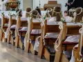 Dzieci w bieli, z wiankami na głowach, siedzą w ławkach kościelnych. Czekają na uroczystość, zastanawiając się, ile trwa komunia w kościele.