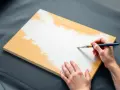 Une main applique une couche de peinture blanche sur une planche de bois. La question est : peut-on vernir par dessus du vernis ?