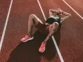 Atleta esausto sdraiato su una pista da corsa, con le mani sulla testa, forse vittima della sindrome da overtraining.