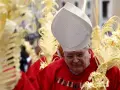 A bishop in red vestments and a white mitre holds a palm frond, surrounded by others. This scene marks Passion Sunday.