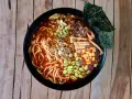 Miseczka aromatycznych dań z makaronem ramen, pełna edamame, kukurydzy, grzybów i nori, na drewnianym tle.