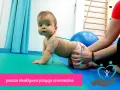 Niemowlę w pozycji czworaczej, z rękami opartymi na macie. Fizjoterapeuta delikatnie wspiera jego biodra.