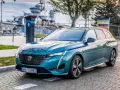 Turkusowe kombi Peugeot 308 zaparkowane na bruku, w tle okręt wojenny.
