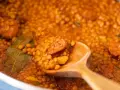 Primer plano de lentejas con chorizo y laurel en una cuchara de madera.
