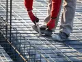 Budowlaniec wiąże zbrojenie. To kluczowy etap budowy, który wpływa na to, ile stali na dom 100m2 będzie potrzebne.