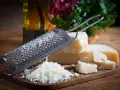 Tarka z kawałkami sera **padano ser** i świeżo startym serem. Obok butelka oliwy i zielenina.