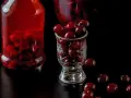 Butelka i kieliszek wypełnione wiśniami, obok kilka luźnych owoców. To nalewka z wiśni z pestkami, gotowa do degustacji.
