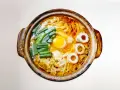 Gorący garnek z aromatycznym bulionem, żółtkiem jajka, zielonym szczypiorkiem i krążkami rybnymi. Czy to ramen czy udon?