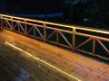 Träaltan med staket upplyst av varma decklights. En grill står på altanen.