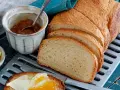 Ein Laib **sauerteig Toastbrot** ist aufgeschnitten. Daneben stehen Marmelade, Butter und ein Messer mit einem Stück Brot, das bestrichen ist.