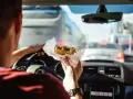 Uomo al volante mangia un panino in un ingorgo. Si può mangiare mentre si guida, ma attenzione alla sicurezza!