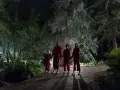 Cztery postacie w czerwonych kombinezonach stoją na drewnianym tarasie nocą. Ich obecność zapowiada mroczny plot filmu.