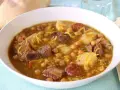 Un reconfortante rancho canario en un cuenco blanco, con garbanzos, trozos de carne, patatas y fideos finos.