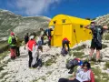 Gruppo di escursionisti vicino a un giallo blockhaus Majella, su un sentiero roccioso con montagne verdi sullo sfondo.