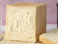 Un pain de mie moelleux, parfait pour une recette facile. Un pot de farine et un moule à pain sont à proximité.