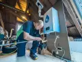 Installazione di caldaie a idrogeno in un sottotetto. Un tecnico collega tubi a un'unità bianca con il simbolo H2.