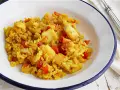 Arroz amarillo con trozos de bacalao y pimientos rojos en un plato blanco.