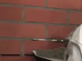 Prace przy ścianie z cegły klinkierowej. Narzędzie do fugowania zbiera zaprawę, przygotowując do czyszczenia klinkieru.