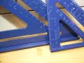 Niebieskie kątowniki stolarskie, jeden z nich z napisem "ALUMINUM SQUARE", leżą na drewnianym blacie.