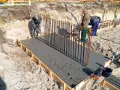 Budowa fundamentów: pracownicy wylewają beton, przygotowując zbrojenie pod przyszły żelbeton.