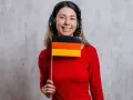 Uśmiechnięta kobieta w słuchawkach trzyma flagę Niemiec. Czy to jej nowy nauczyciel języka niemieckiego?