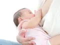 Malutkie dziecko w różowo-białe paski pije mleko mamy. To piękny moment karmienia, kiedy pojawia się nawał pokarmu.