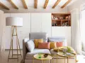 Sofá gris con cojines coloridos, mesa auxiliar amarilla y lámpara de pie. Ideas para decorar piso alquiler low cost con estilo y calidez.
